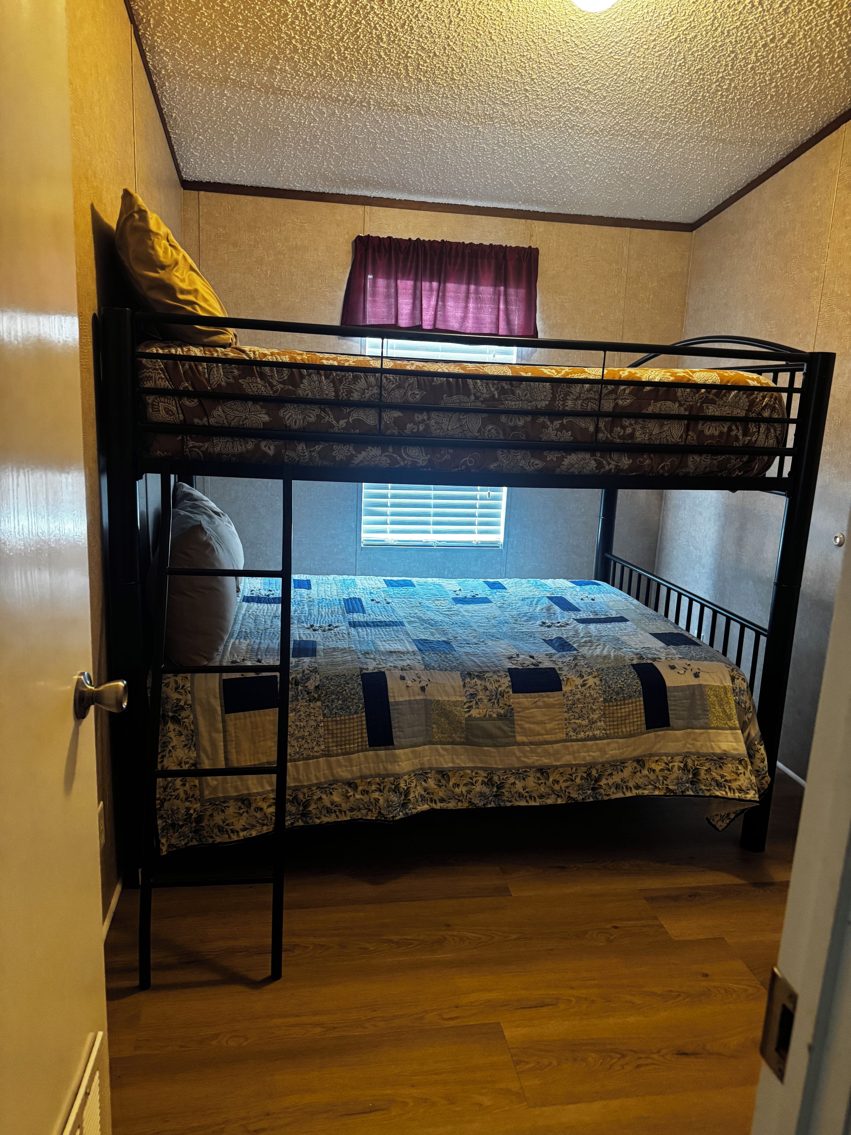 Una cama litera con colcha, una ventana con persianas y una puerta con manija.