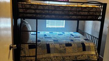 Una cama litera con colcha, una ventana con persianas y una puerta con manija.