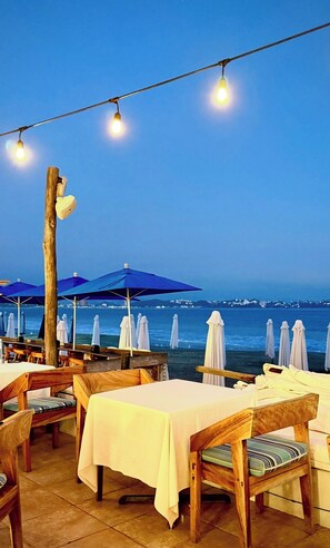 An outdoor seating area with tables and chairs, umbrellas, and a view of the sea. - Charming 2-bedroom bed & breakfast with AC in Manzanillo on a golf course! (Manzanillo)