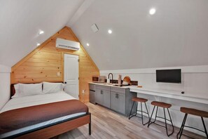 A bedroom with a bed, a wooden ceiling, a kitchenette with a microwave, and a TV mounted on the wall. - PA Grand Canyon Cozy Cabin (Wellsboro)