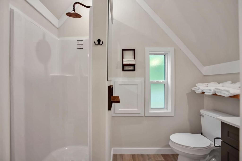 A bathroom with a shower, toilet, and a small window.