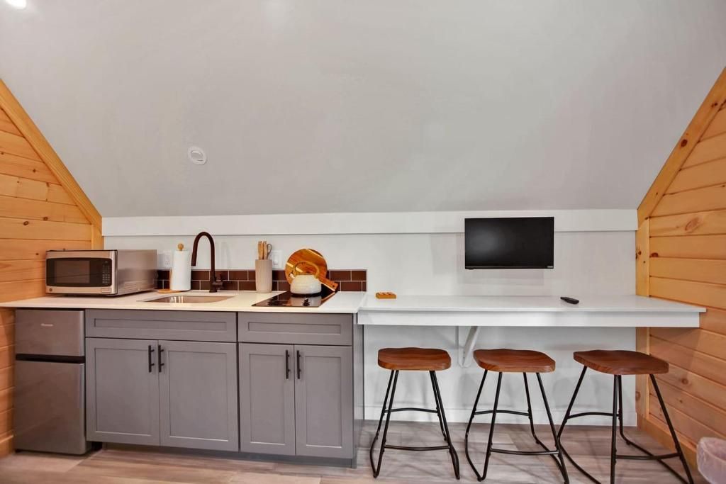 A compact kitchen with a microwave, sink, and a flat-screen TV. There are three stools at the counter.