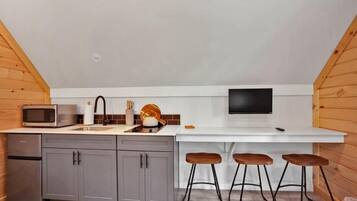 A compact kitchen with a microwave, sink, and a flat-screen TV. There are three stools at the counter.