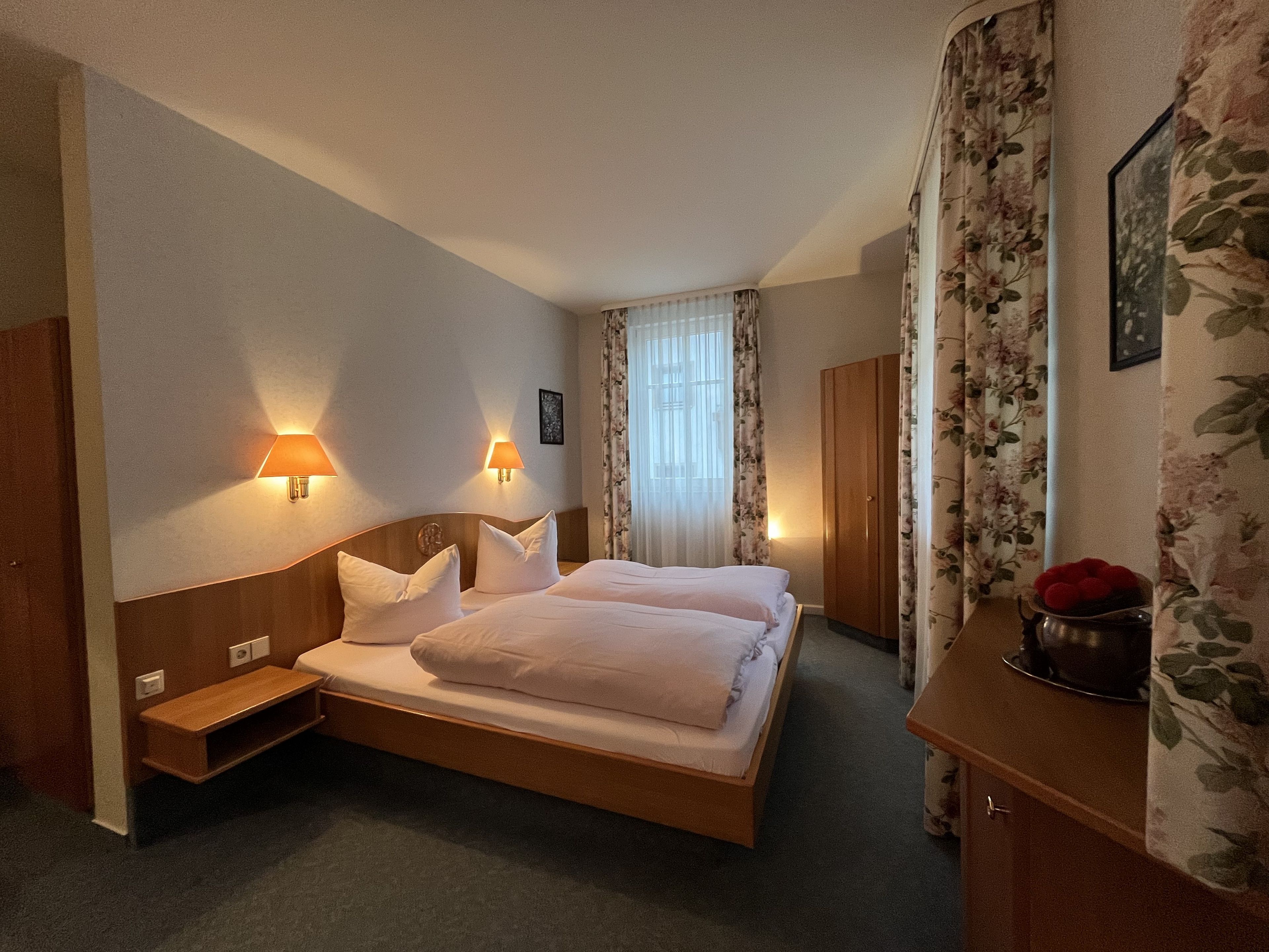 Camera d'albergo con un letto matrimoniale, due lampade ai comodini, un armadio, un tavolino e uno specchio.