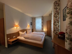 Camera d'albergo con un letto matrimoniale, due lampade ai comodini, un armadio, un tavolino e uno specchio.