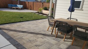 Une terrasse avec un sol en pierre, une table en bois et des chaises en osier.