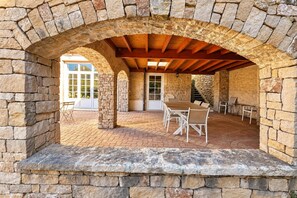 Un espace extérieur aménagé en terrasse, avec des murs en pierre, des poutres en bois et une table entourée de chaises.