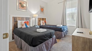 Habitación de hotel con dos camas, un escritorio, una lámpara y obras de arte en las paredes.