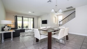A modern dining area with a glass table, white chairs, and a flat-screen TV mounted on the wall.