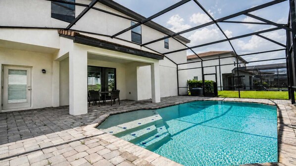 A modern house with a swimming pool, a covered patio, and a view of neighboring houses.