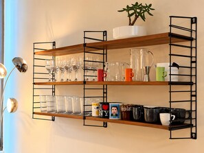 A wall-mounted shelving unit with multiple tiers holding glassware, mugs, and decorative items. - Rue Isidoor Teirlinck 18 (Molenbeek-Saint-Jean)