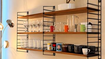Une étagère murale à plusieurs niveaux, conçue pour exposer des verres, des tasses et des objets décoratifs.