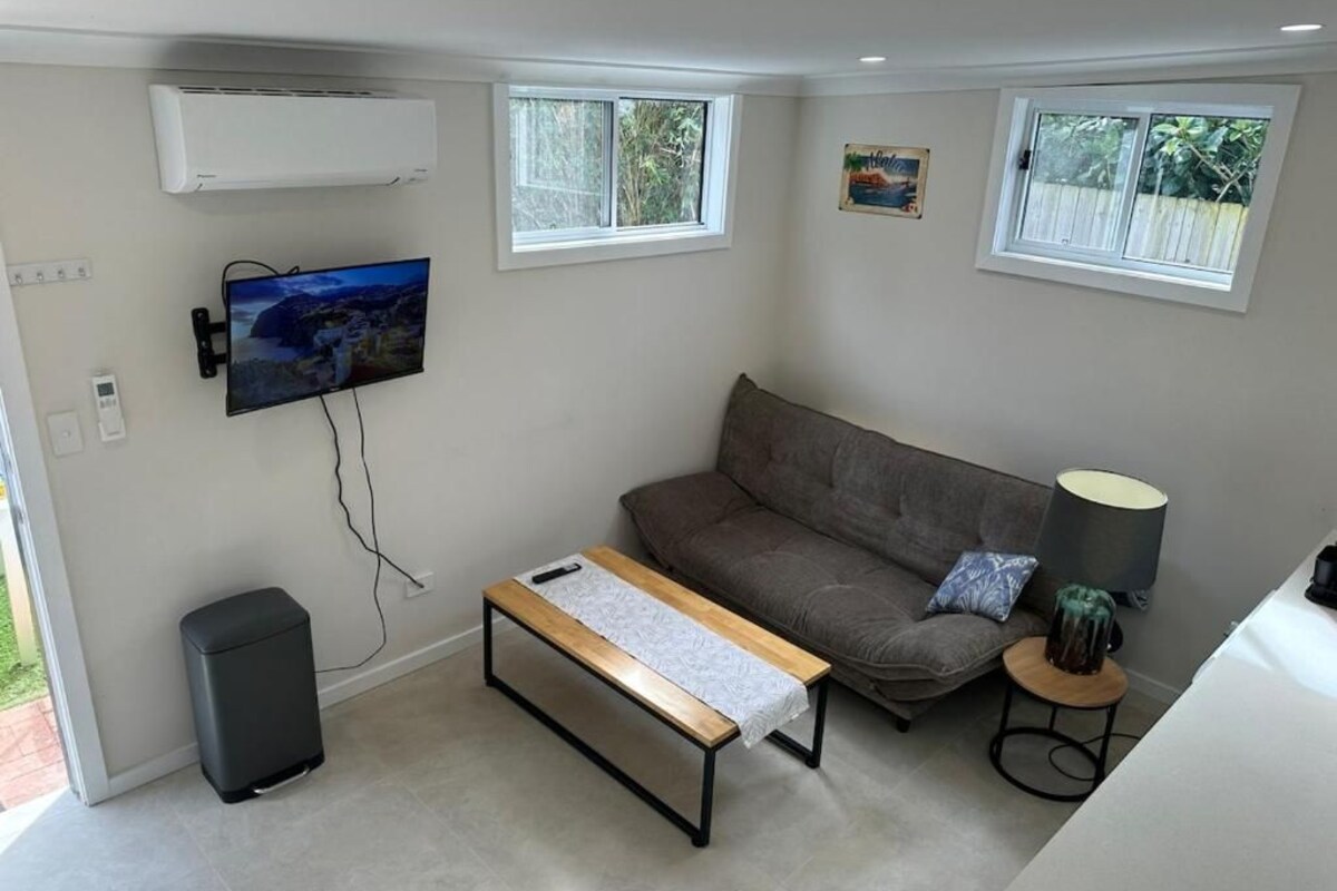 A living room with a sofa, a coffee table, a TV mounted on the wall, and a small table with a lamp.