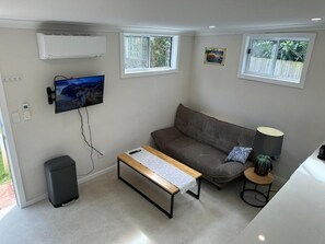 A living room with a sofa, a coffee table, a TV mounted on the wall, and a small table with a lamp. - 33 Adams St (Curl Curl)