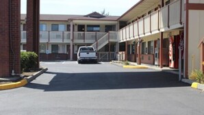 Un motel con una zona de estacionamiento central, un pasillo cubierto y un edificio de dos pisos con balcones.