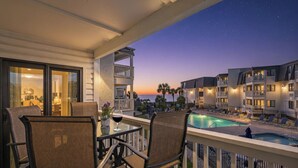 A balcony with a pool, chairs, and a view of the ocean at dusk. - Ocean Forest Villas by Elliott Beach Rentals (Myrtle Beach)