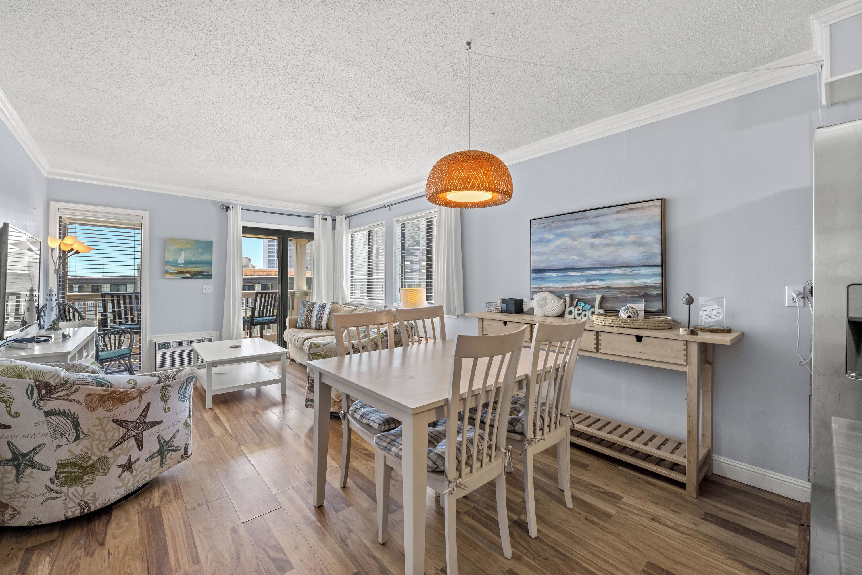 Un comedor con una mesa y sillas de madera, una lámpara colgante y vistas al exterior a través de amplios ventanales.
