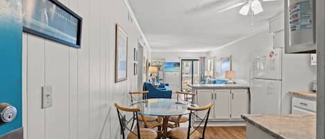 A modern kitchen with white cabinets, a round glass table, and wicker chairs.