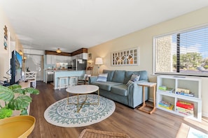 A living room with a sofa, coffee table, and a small side table. There is a kitchen in the background with white cabinets and a dining area. - Ocean Forest Villas by Elliott Beach Rentals (Myrtle Beach)