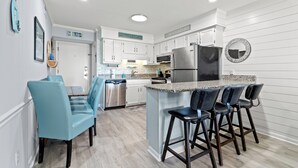 A modern kitchen with white cabinetry, a granite countertop, and a central island with bar stools. - Ocean Forest Villas by Elliott Beach Rentals (Myrtle Beach)