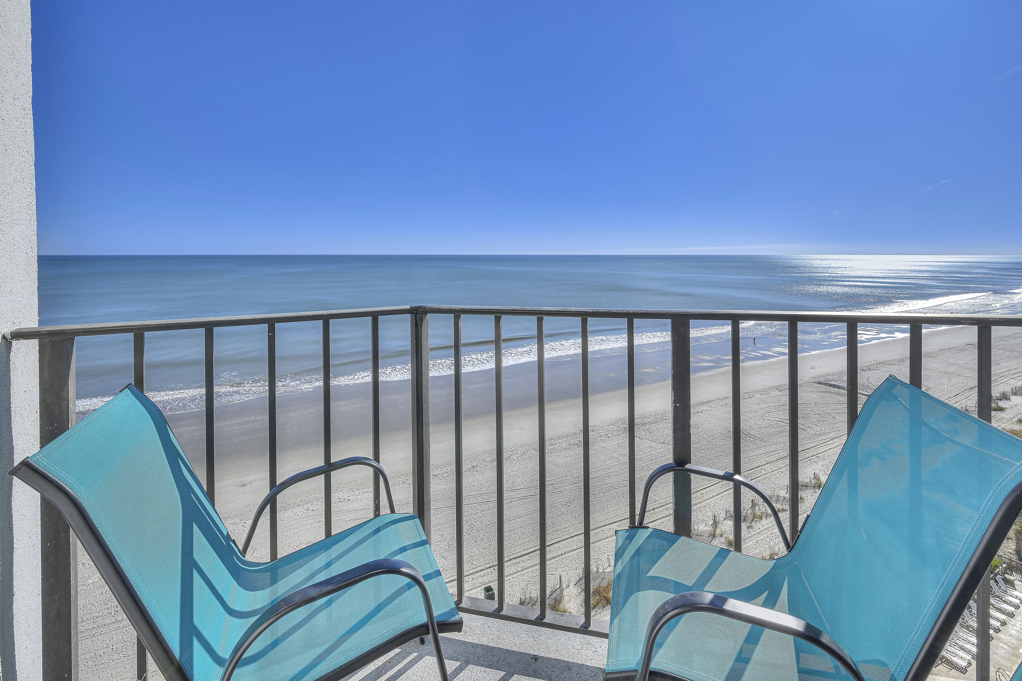 Un balcon avec deux chaises bleues donnant sur une plage.