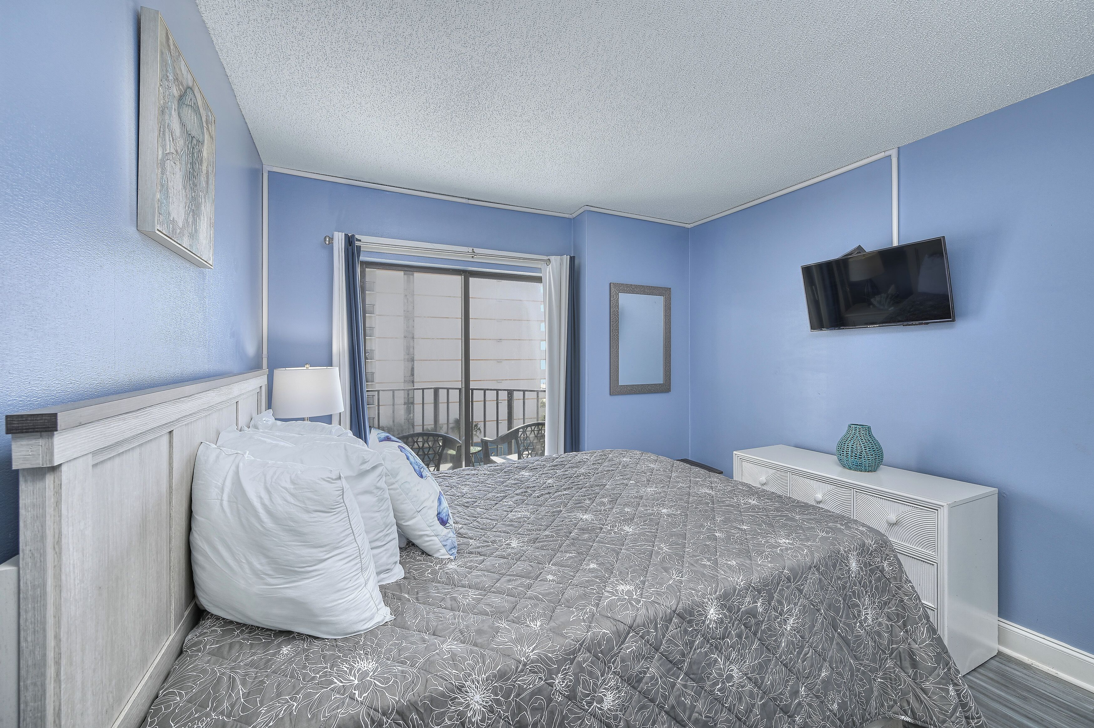 A bedroom with a bed, a dresser, a TV, and a window with blinds.