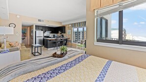 Quarto de hotel moderno com cama grande, cozinha compacta, área de refeições e vista para a cidade.