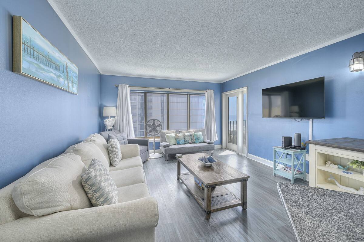 A living room with a sofa, coffee table, and a flat-screen TV mounted on the wall.