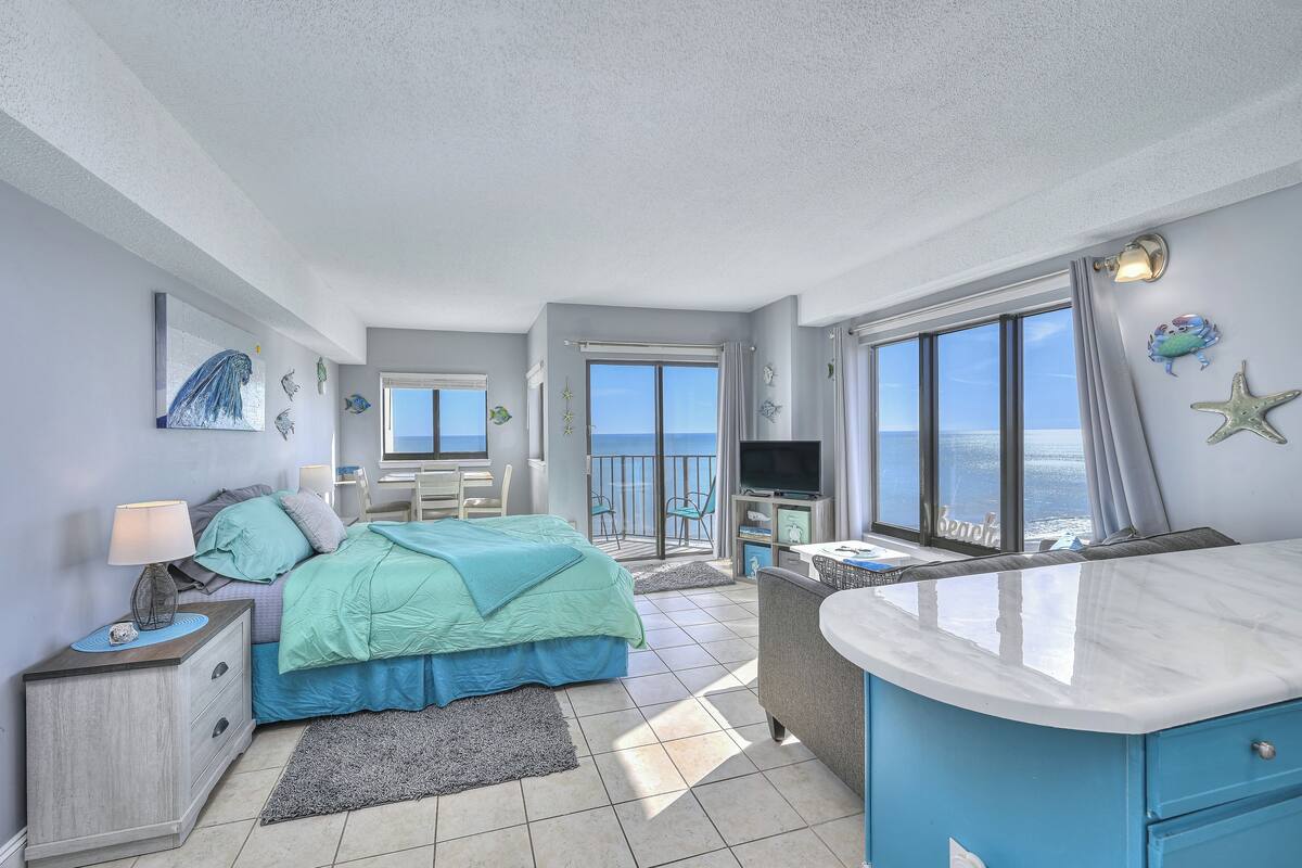 A bedroom with a bed, a nightstand, a TV, and a view of the sea.
