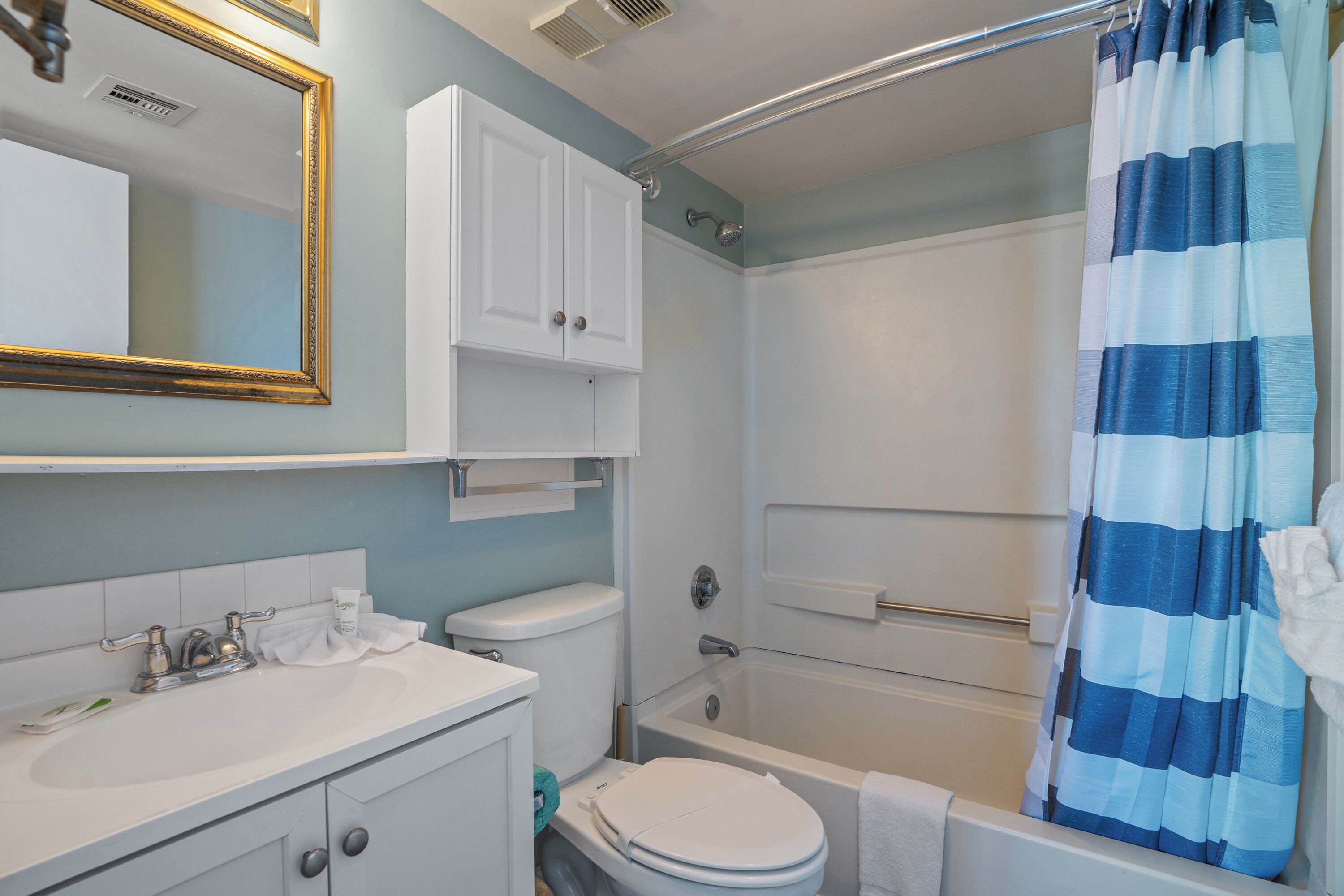A bathroom with a white sink, toilet, and bathtub. There is a shower curtain and a towel rack.