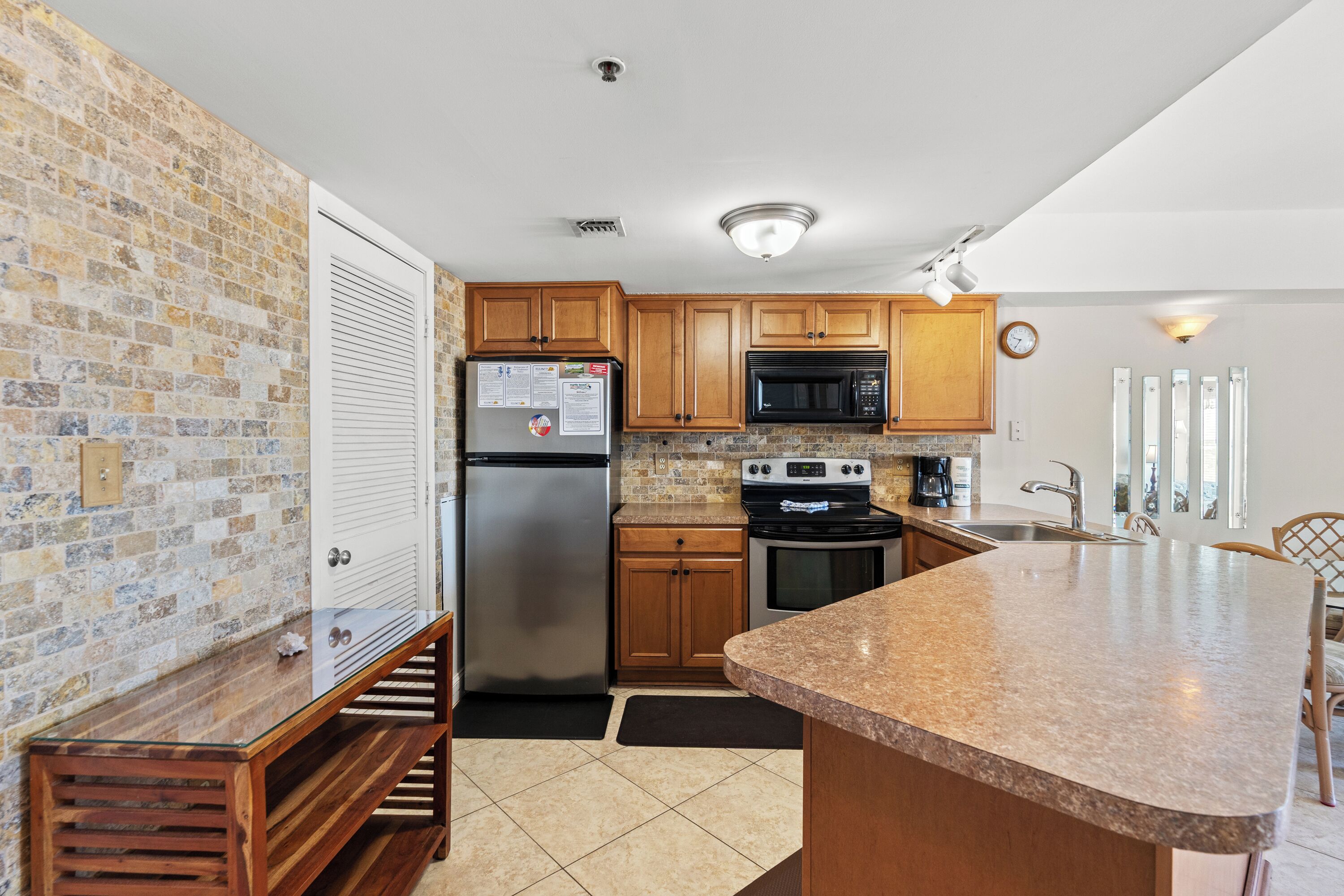 A kitchen with a brick wall, wooden cabinets, stainless steel appliances, and a granite countertop.