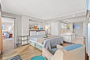 A modern bedroom with a bed, bedside table, and a bathroom with a bathtub. - Units at Caravelle Resort by Elliott Beach Rentals (Myrtle Beach)
