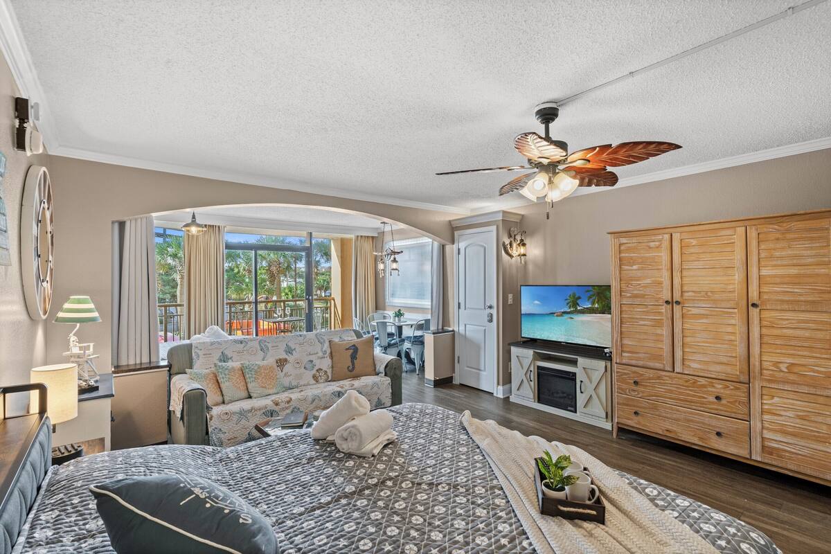 A spacious bedroom with a large bed, a ceiling fan, a TV, and a wooden wardrobe.