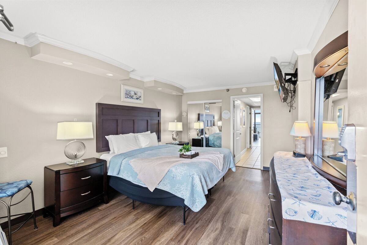 A hotel room with a bed, bedside tables, a mirror, and a view into the hallway.