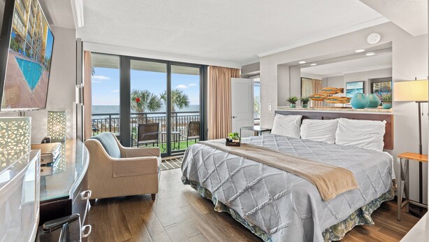 A hotel room with a large bed, a desk, a chair, and a balcony with a view of the ocean. - Units at Caravelle Resort by Elliott Beach Rentals (Myrtle Beach)