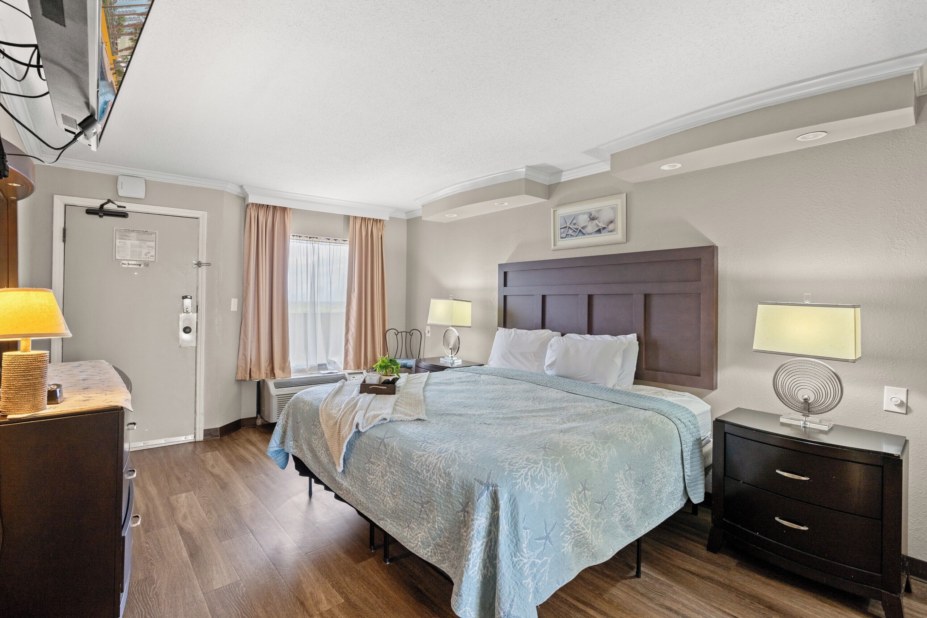A hotel room with a bed, bedside tables, a dresser, a desk, and a window with curtains.