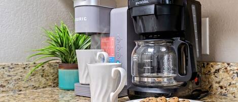 Een keuken met een koffiezetapparaat, een witte mok, een bord met koekjes en een potplant.