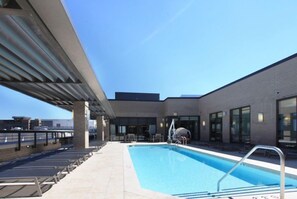 A rooftop swimming pool with lounge chairs, a covered seating area, and a view of the city skyline.