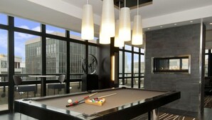 A modern indoor pool table with a billiard cue and balls, a fireplace, and large windows offering a city view. - Sedona-Slate by Executive Apartments (Arlington)