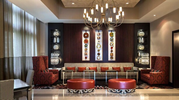 A lobby with a modern chandelier, a sofa with red cushions, and a wall with decorative plates. - Sedona-Slate by Executive Apartments (Arlington)
