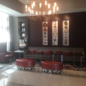 A modern lobby with a chandelier, a sofa with red cushions, and a wall decorated with various plates and vases. - Sedona-Slate by Executive Apartments (Arlington)