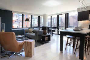 A modern apartment with a living area, kitchen, and dining space. It features large windows, a sofa, a coffee table, and a dining bar.