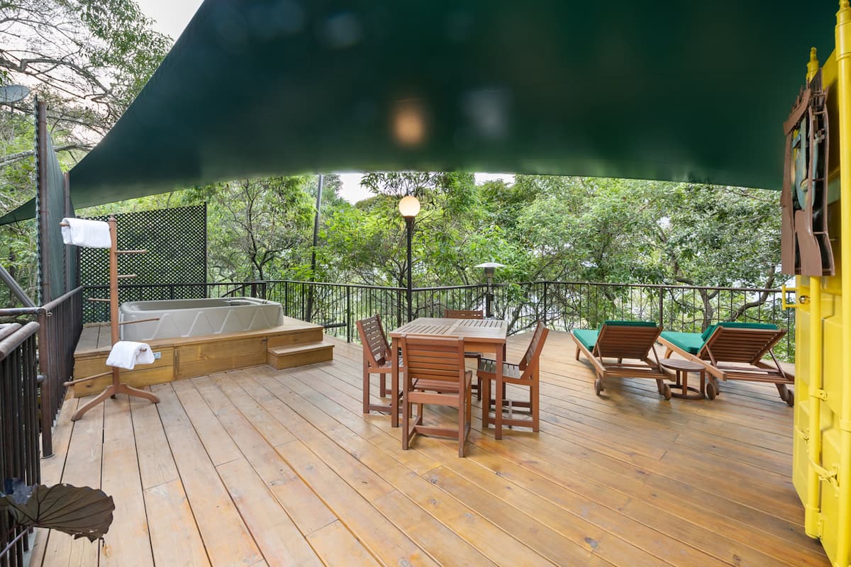 Una terraza de madera con una mesa y sillas, un jacuzzi y sillones de descanso.
