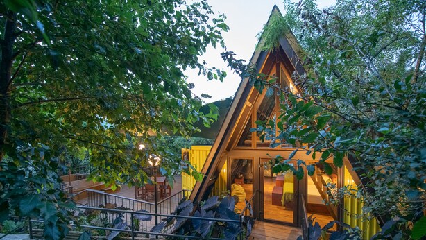 A modern, triangular wooden structure with a glass entrance, surrounded by lush greenery. - Santo Cielo by Casa Santo Domingo (Antigua Guatemala)