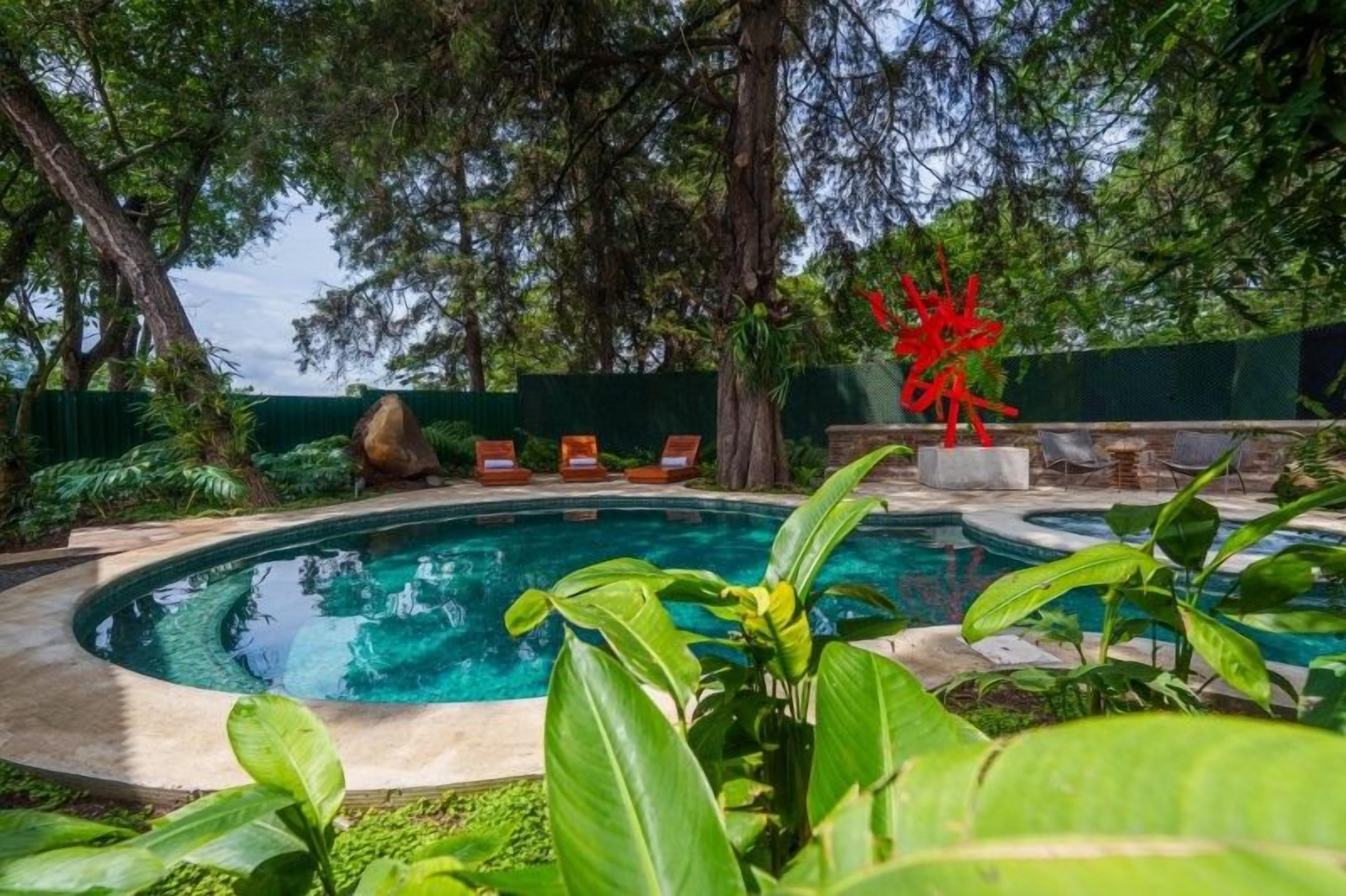 A swimming pool with a surrounding garden, a red sculpture, and lounge chairs.