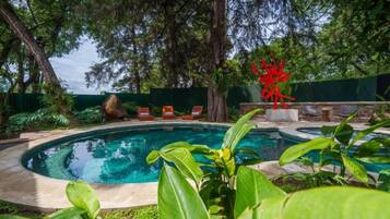A swimming pool with a surrounding garden, a red sculpture, and lounge chairs.