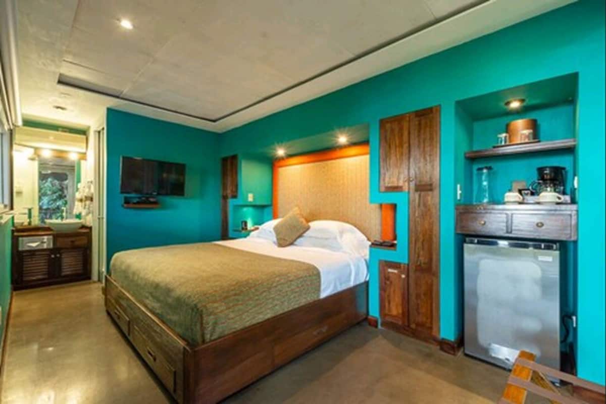 Un dormitorio con cama, mesita de noche, cómoda, escritorio integrado y refrigerador.