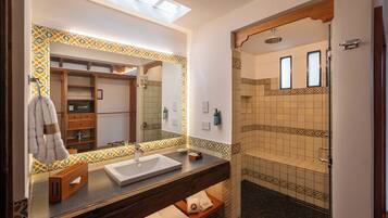 A bathroom with a large mirror, a sink, a towel rack, a shower area, and a wooden shelf.