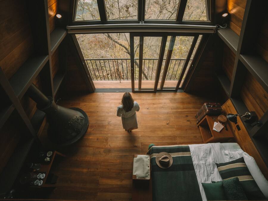 Una habitación amplia con un gran ventanal, una cama, una maleta y suelo de madera.