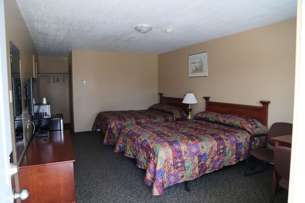 Une chambre d’hôtel avec deux lits, un bureau, une chaise, une lampe et un tableau au mur.